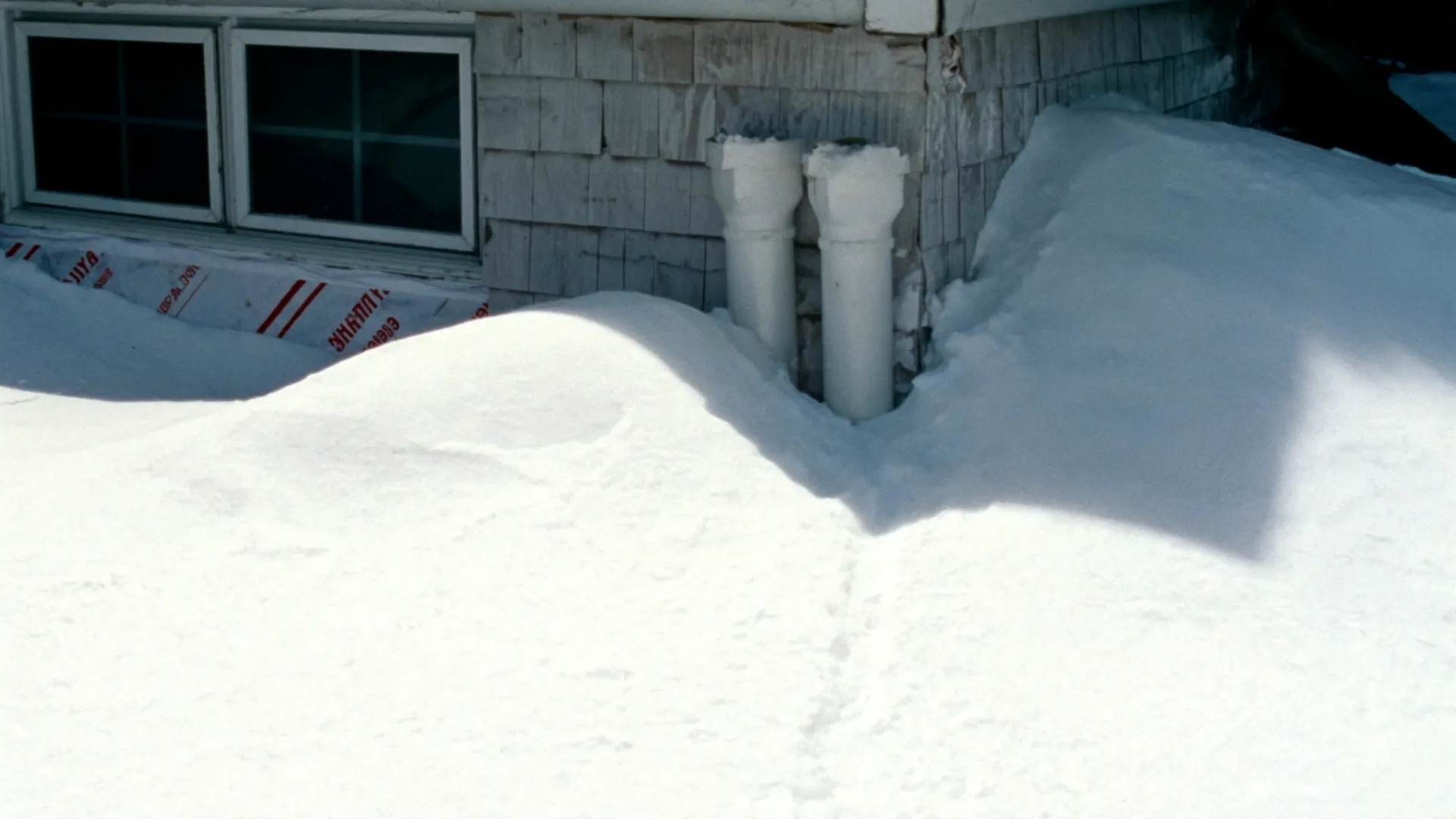 Two white PVC vent pipes with a snow drift built up against them